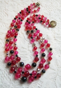 image shows a triple strand beaded bib necklace, made up of 3 rows of red and pink plastic beads