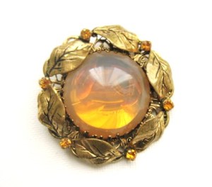 Image shows a large round brooch, with amber color opalite centre glass stone, surrounded by metal leaves in gold tone metal, and signed West Germany on the reverse