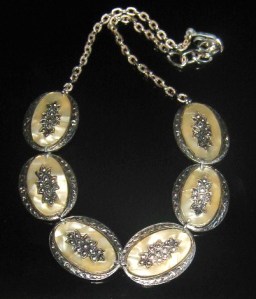 Photo shows an Eloxal metal necklace, made from 6 oval panels decorated with plastic faux mother of pearl, attached to a chain
